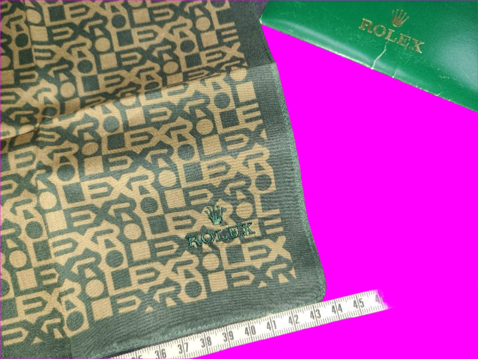 Green fabric with Rolex logo and a measuring tape for scale on a dark background